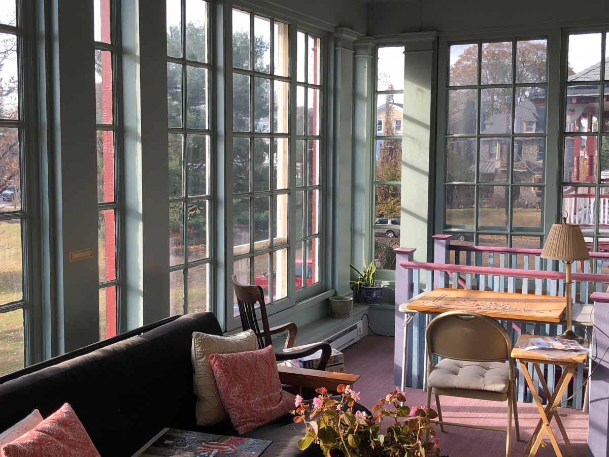 A cozy sunroom filled with natural light, featuring a sofa, chairs, and a table surrounded by large windows.