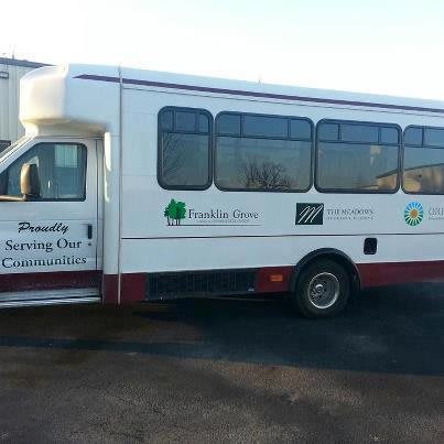 A community service shuttle bus parked, featuring logos on its side.