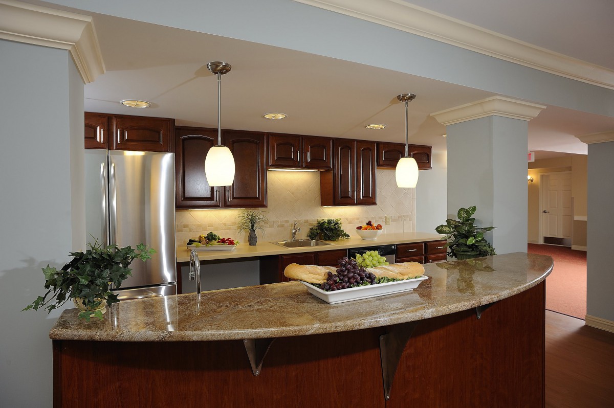 A modern kitchen featuring wood cabinets, marble countertops, and stainless steel appliances with pendant lighting.