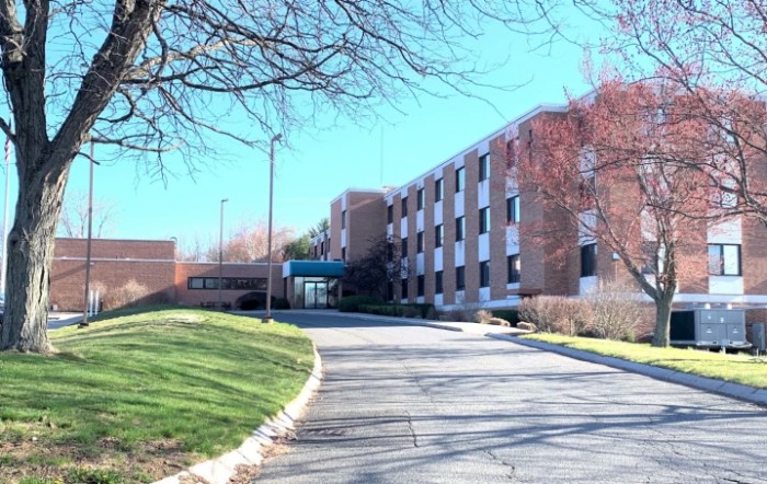 A multi-story brick building with a driveway and surrounding trees.