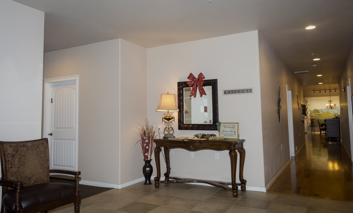 A cozy living room corner featuring a decorative table with a mirror above, adorned with a bow, and accompanied by a lamp and flower vase.