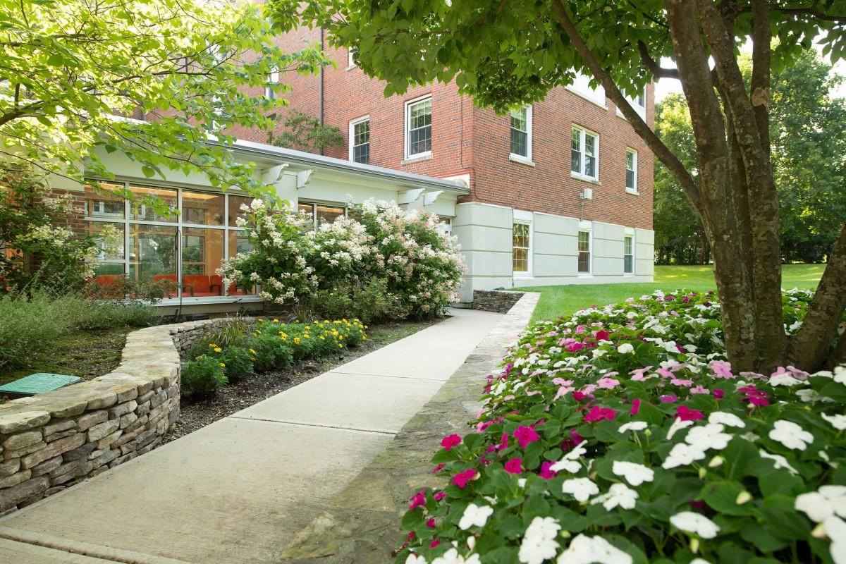 A scenic view of a building with a pathway surrounded by lush greenery and colorful flowers.