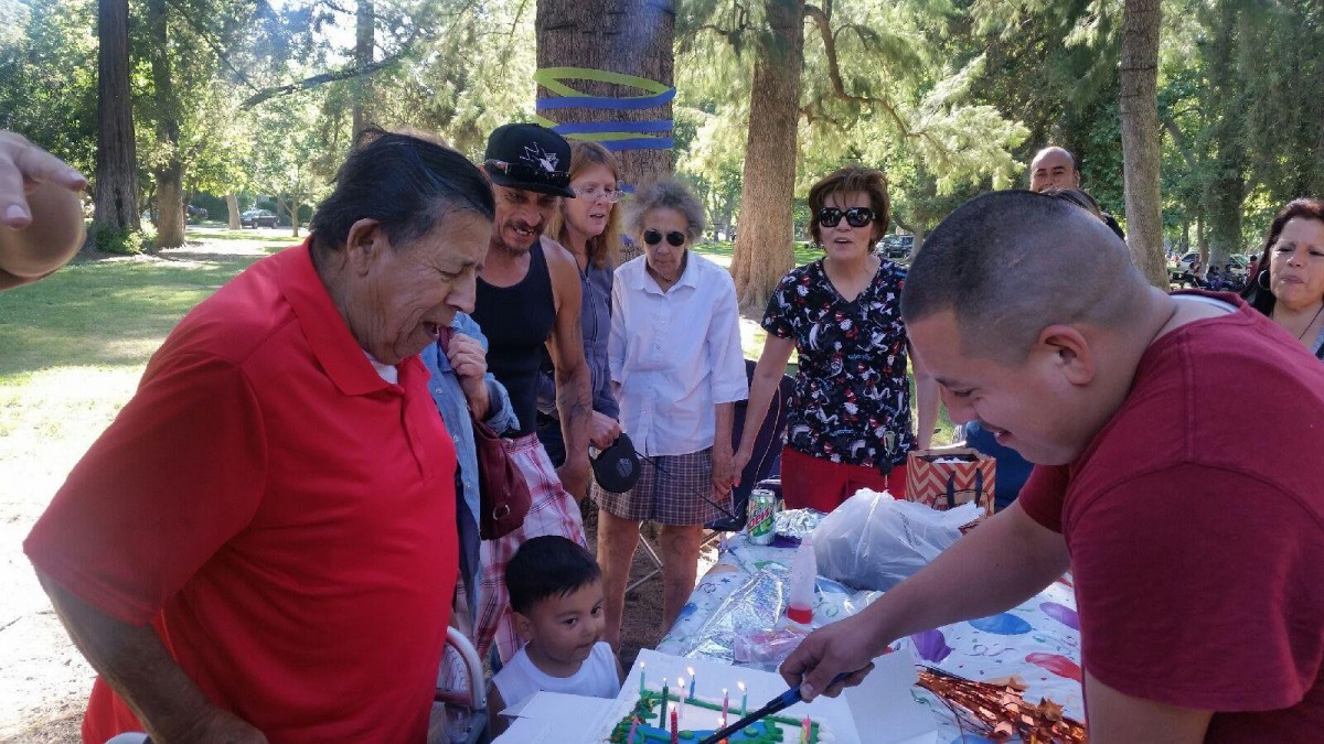 A family gathered outdoors celebrating a birthday with a cake.