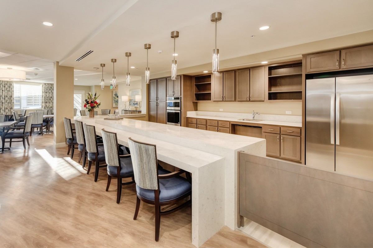 A modern open-concept kitchen with a large island and dining area, featuring pendant lighting and wood flooring.