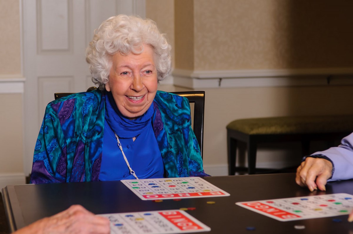 An elderly woman smiling while playing bingo indoors.