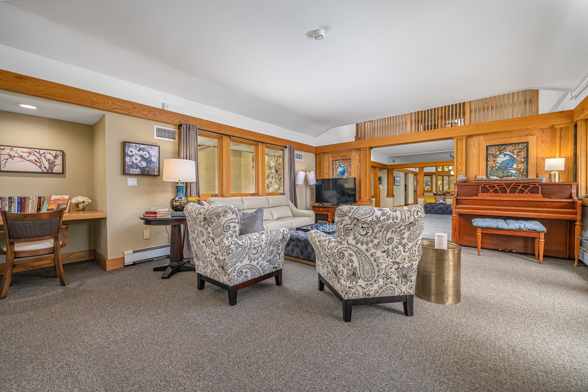 A cozy living room with comfortable seating, featuring a couch and armchairs, arranged around a central coffee table. The space is accented with wood paneling and a television.