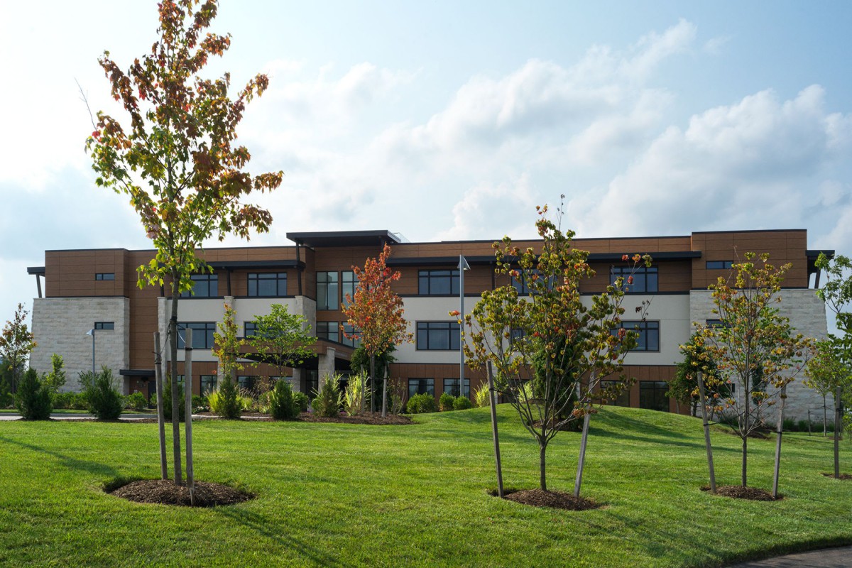 A modern building surrounded by a green lawn and trees under a partly cloudy sky.