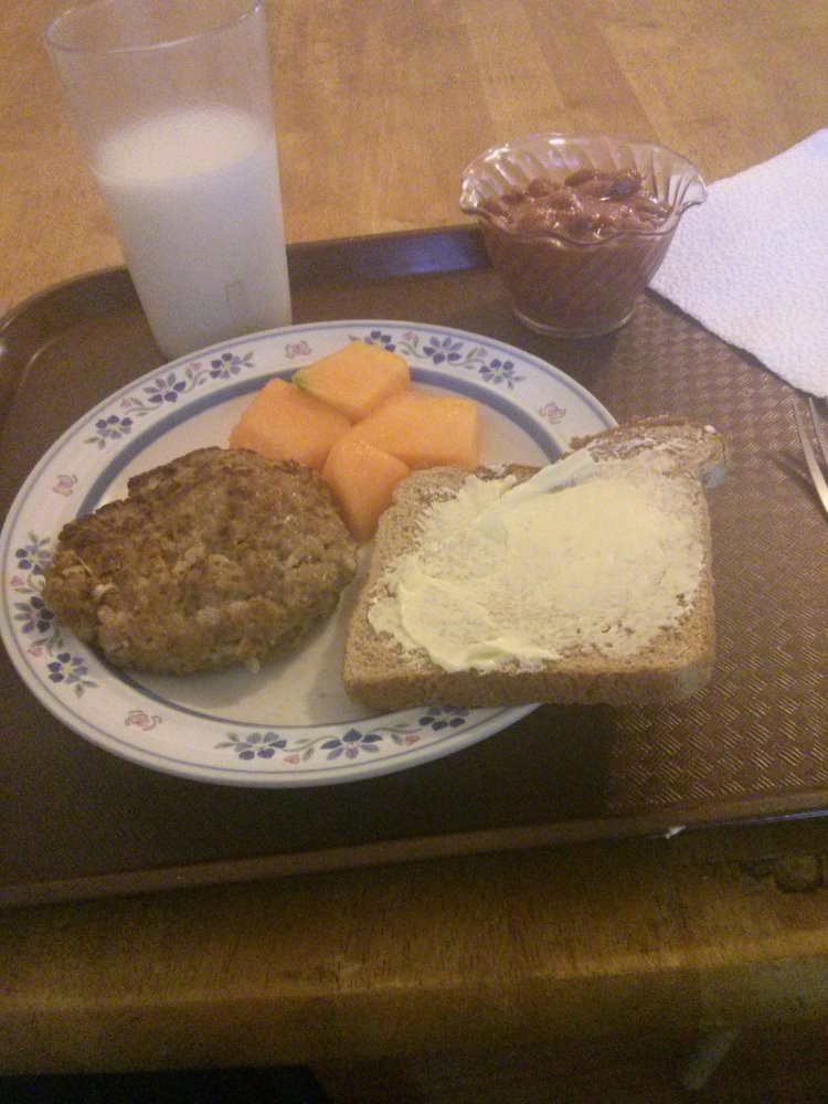 A breakfast tray with buttered bread, cantaloupe slices, a burger patty, and a glass of milk.
