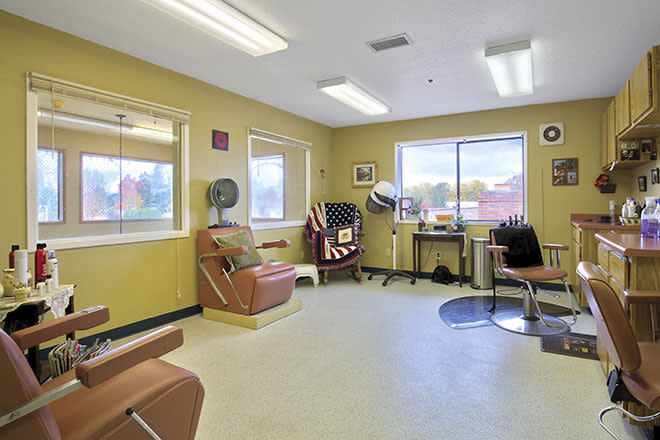 A well-lit waiting room with chairs and armchairs arranged around the space, featuring large windows and overhead fluorescent lighting.