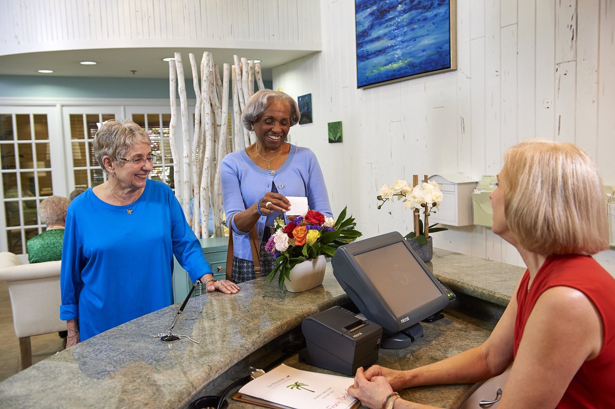 Two elderly women smiling at a receptionist while checking in with a card.