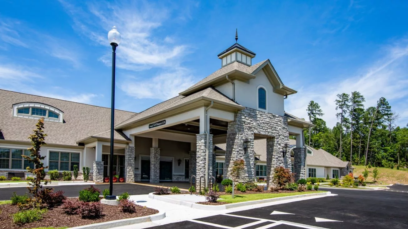 A modern building with a stone facade and landscaped entrance under a clear blue sky.