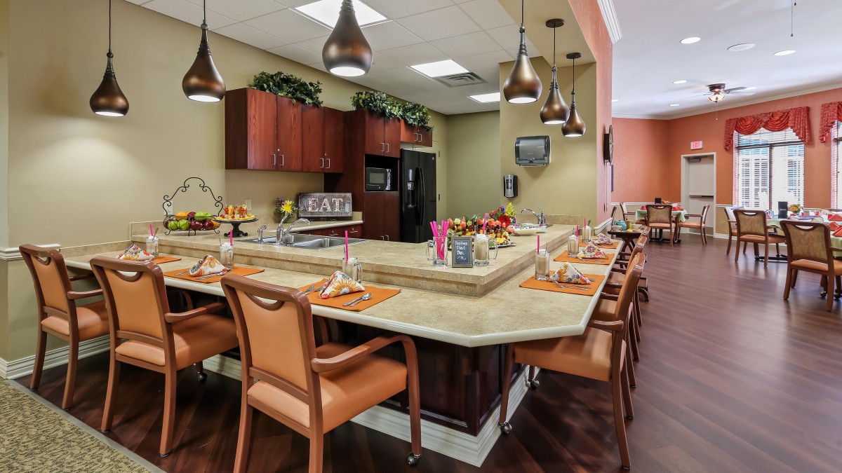 A modern kitchen and dining area featuring a large countertop surrounded by chairs and illuminated by pendant lights.