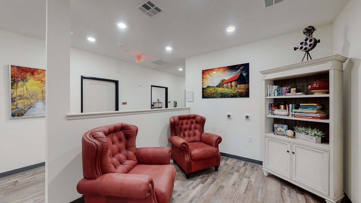A cozy waiting room with two red armchairs and a colorful artwork on the wall.