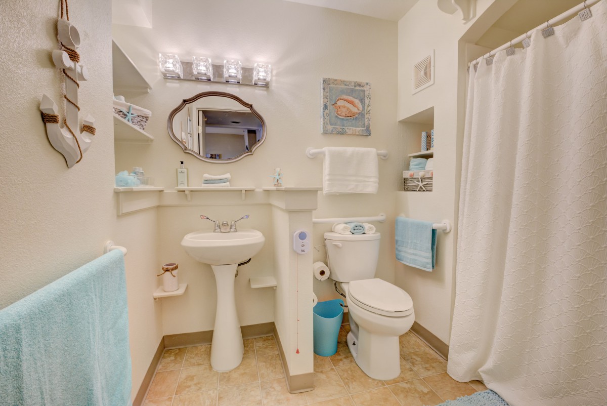A well-organized bathroom with a sink, toilet, and shower, featuring light decor and towels.