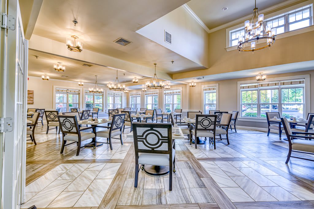 A spacious and elegantly designed dining room with multiple tables and chairs, complemented by large windows and decorative lighting.