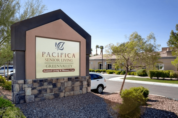 Entrance sign for Pacifica Senior Living Green Valley next to a building and driveway.