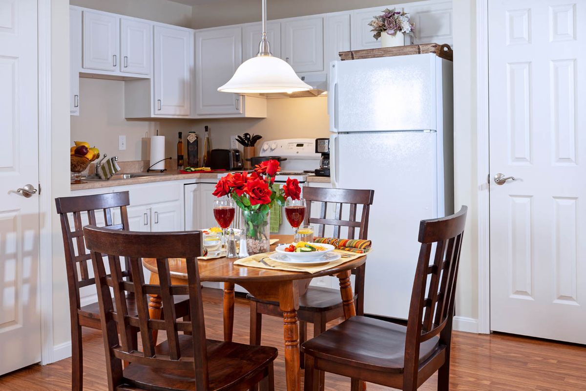 A cozy kitchen with a dining table set for a meal, featuring red flowers and wine glasses.