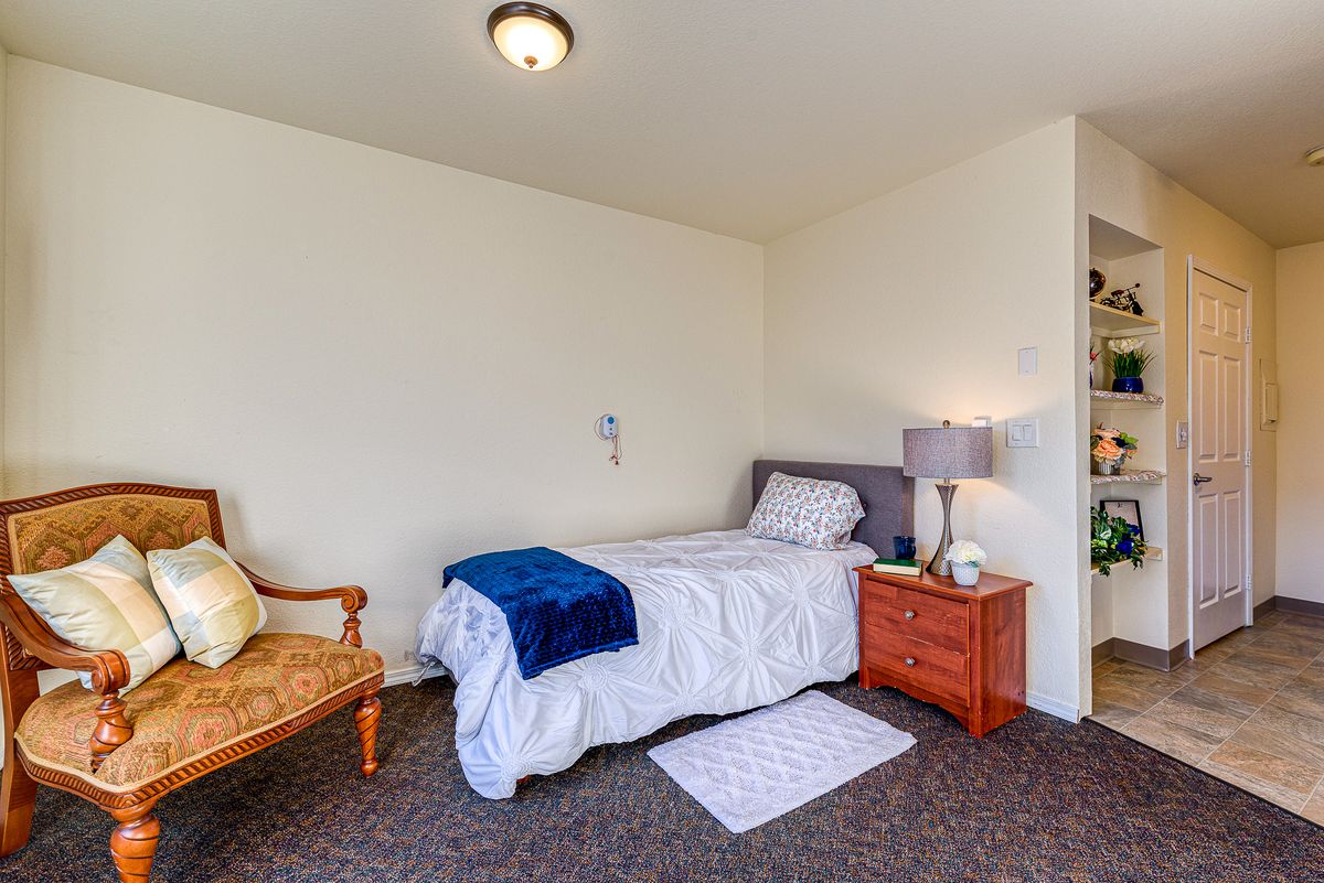 A cozy bedroom with a single bed, nightstand, lamp, and armchair.