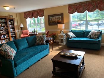 A cozy living room with teal sofas and a wooden coffee table, illuminated by natural light from large windows.