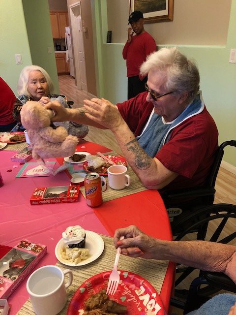 Elderly individuals enjoying a social gathering with cupcakes and stuffed animals.