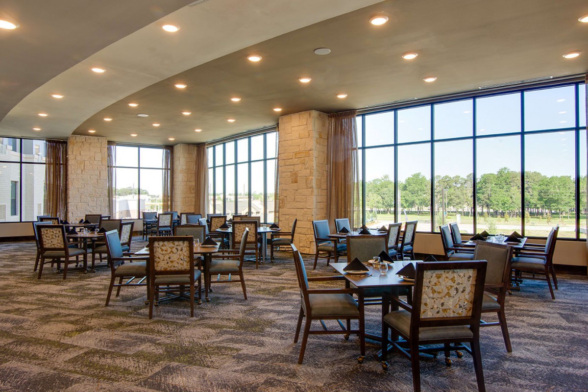 A spacious dining area with large windows allowing natural light to fill the room, furnished with multiple tables and chairs.