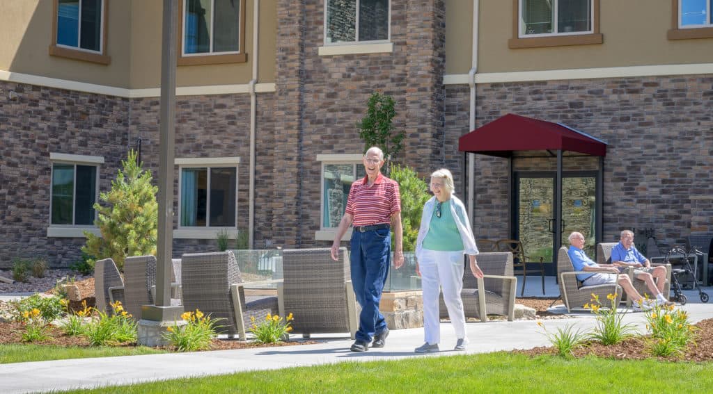 An elderly couple walking together in the garden of a retirement home.