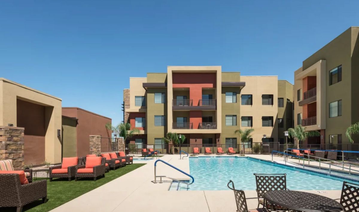 Modern apartment complex with a swimming pool and lounge chairs.