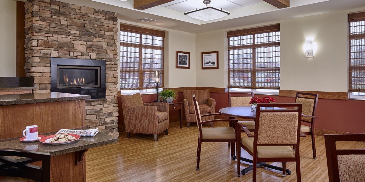 A cozy living room with a fireplace, chairs, wooden floor, and decorative artwork on the walls.