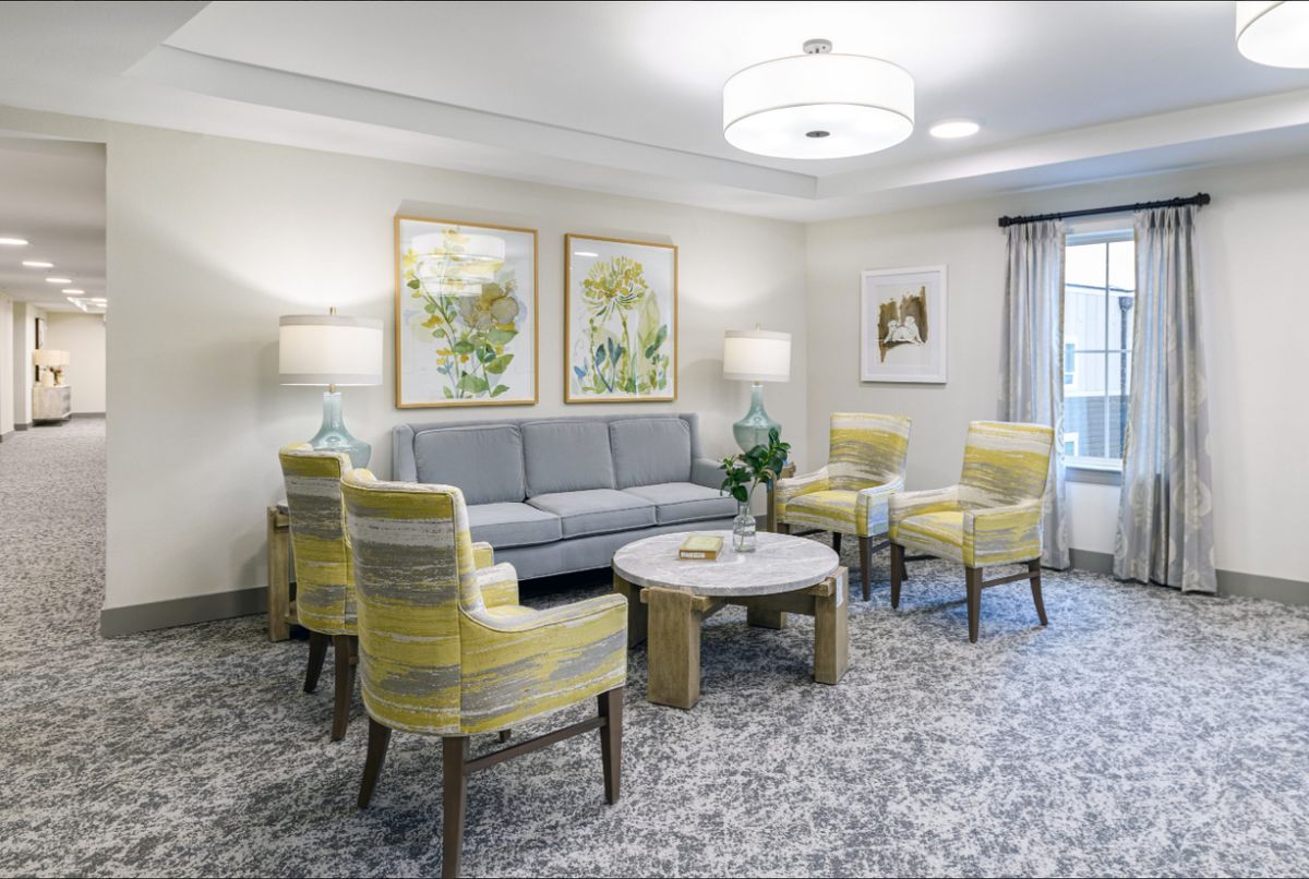 A cozy living room with a modern design featuring a sofa, four yellow chairs, a round coffee table, and decorative artwork on the walls.