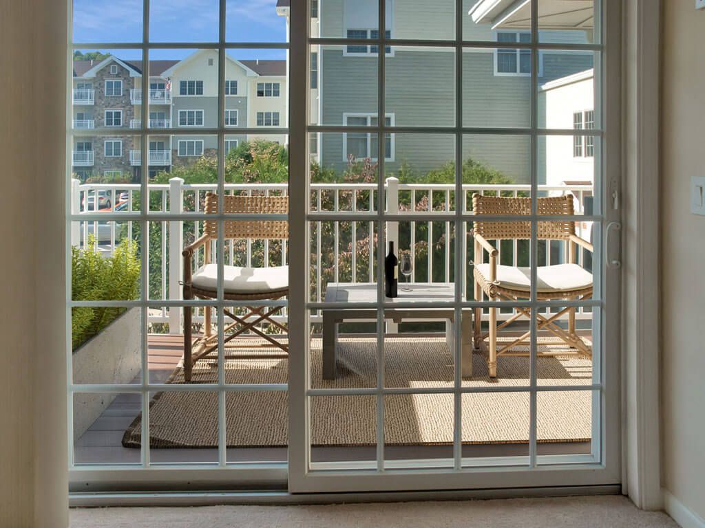 A cozy patio setup viewed through a sliding glass door, featuring two chairs and a small table with a bottle.