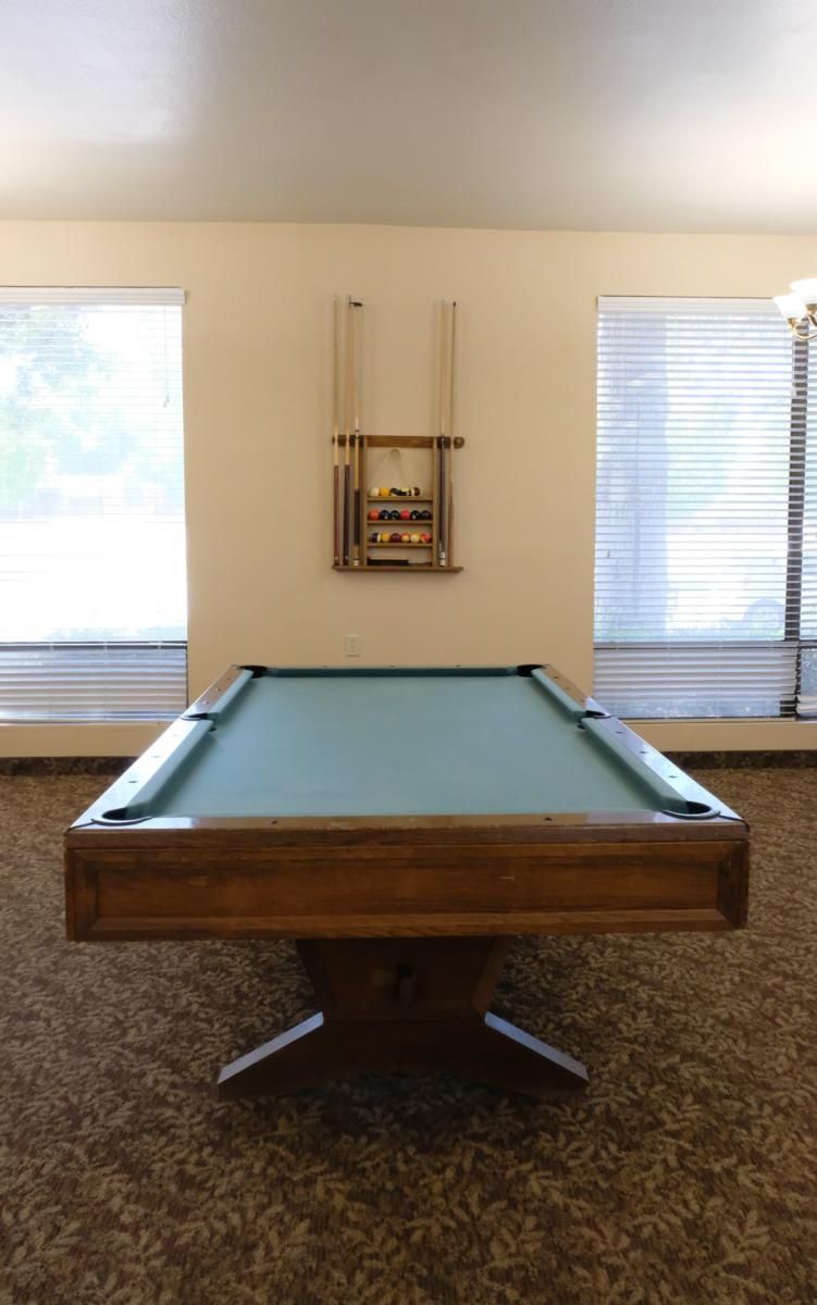 A billiards table in a game room with cue sticks mounted on the wall.