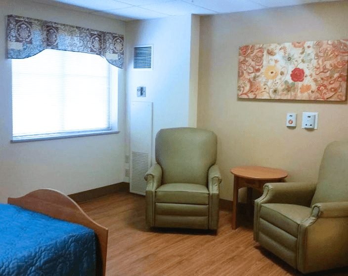 A cozy room interior with two chairs, a bed, and a small table near a window.