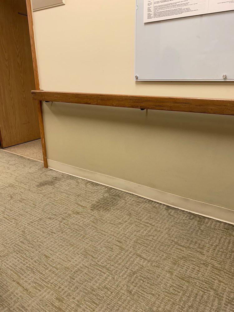An office space with a stained carpet and a whiteboard on the wall.