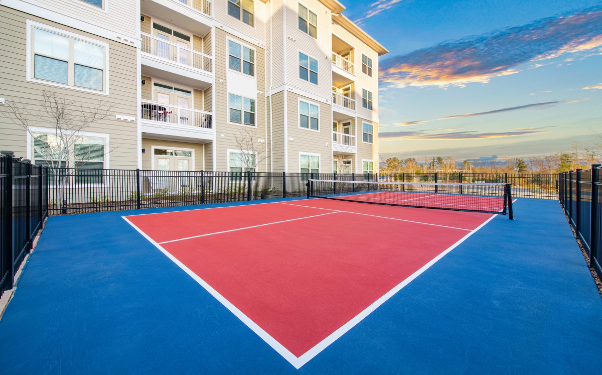 A modern residential building with an outdoor tennis court at sunset.