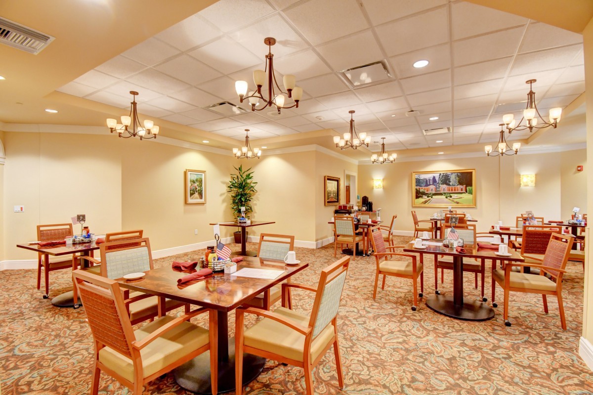 A well-lit dining area with neatly arranged tables and chairs, adorned with chandeliers and decorative wall art.