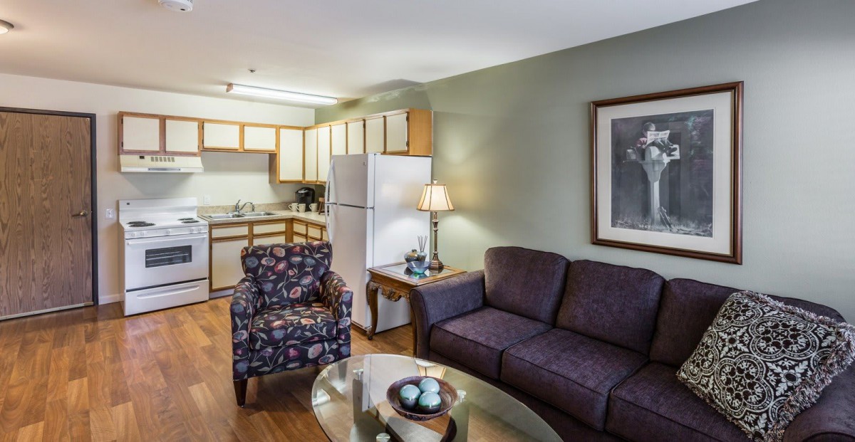 A cozy living room with a connected kitchen area, featuring a sofa, armchair, and modern furnishings.