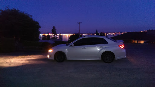 A sleek white car parked by the water under a twilight sky.