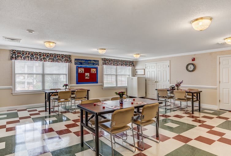 An empty classroom with desks and chairs arranged neatly, featuring bright windows and a patterned floor.