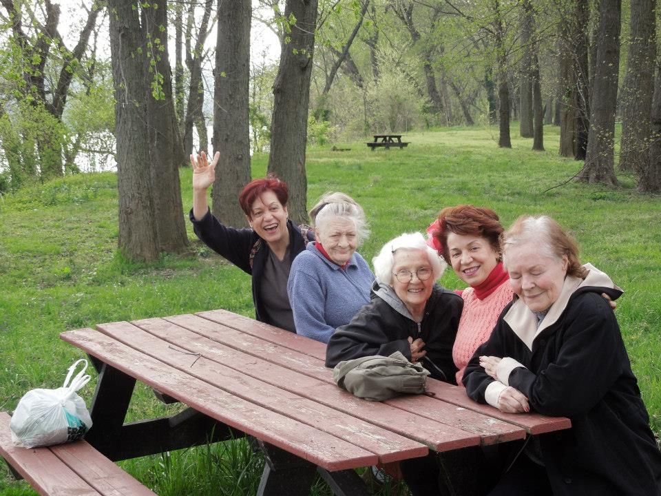 A group of elderly women enjoying a day outdoors at a picnic table in the park.