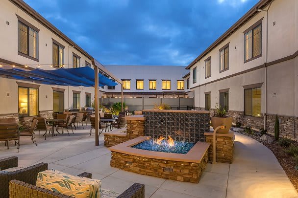 A cozy hotel courtyard with a central fire pit and outdoor seating, illuminated during the evening.
