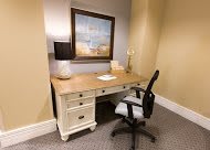A cozy workspace with a wooden desk and office chair, adorned with a lamp and seaside painting.