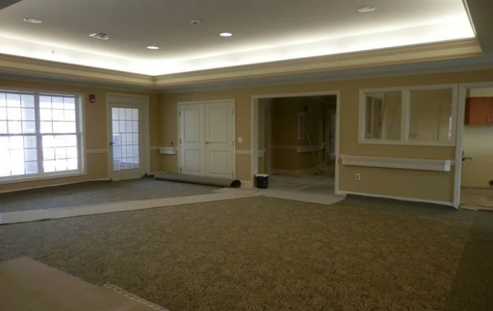 An empty room with carpeted flooring and several doors, illuminated by ceiling lights.
