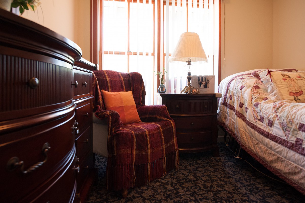A cozy bedroom featuring a plush armchair, wooden dresser, and a neatly made bed.
