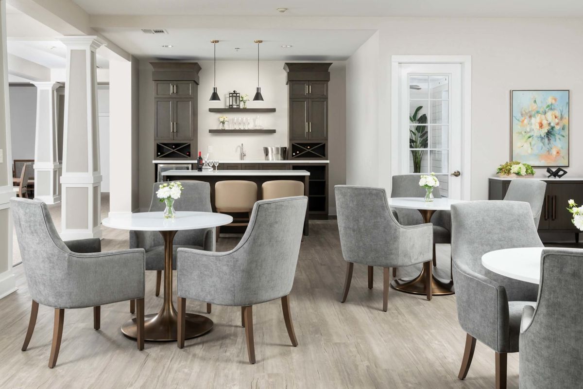 A modern and elegant cafe interior with grey chairs, round tables, and a stylish bar area.