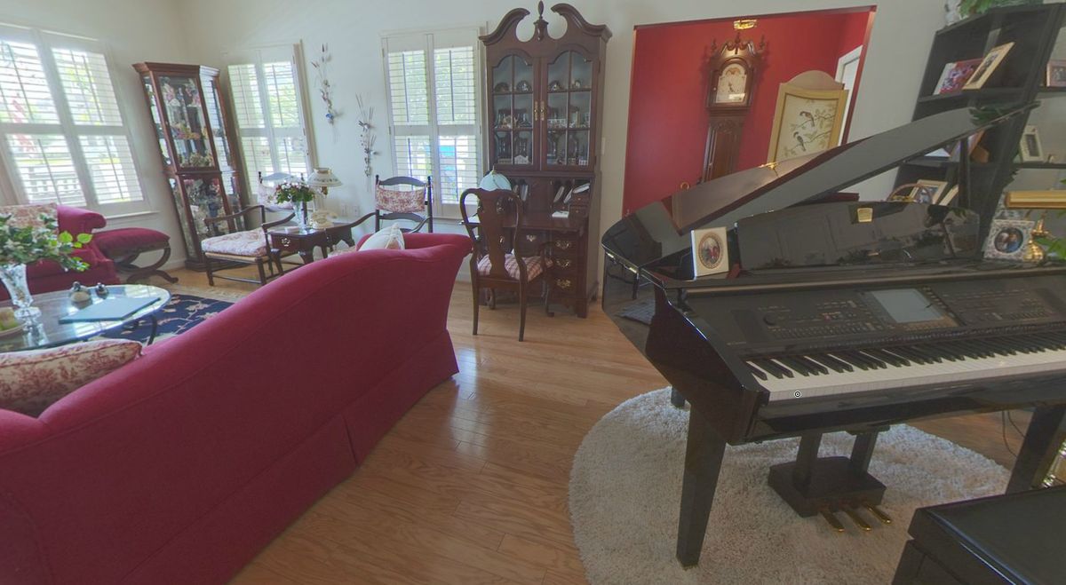 A cozy living room featuring a grand piano, red sofa, and elegant furniture pieces.