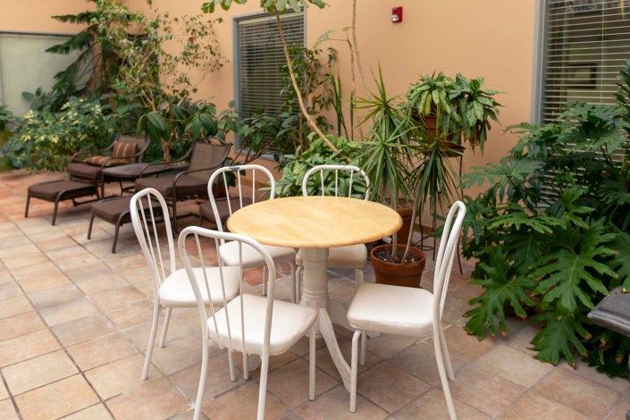 A cozy patio area featuring a round table with four white chairs surrounded by lush green plants.