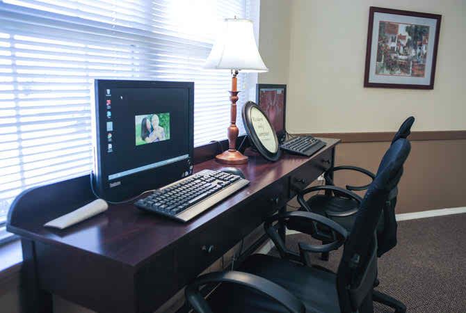 A tidy office workstation with a computer, desk, chair, and lamp by a window.