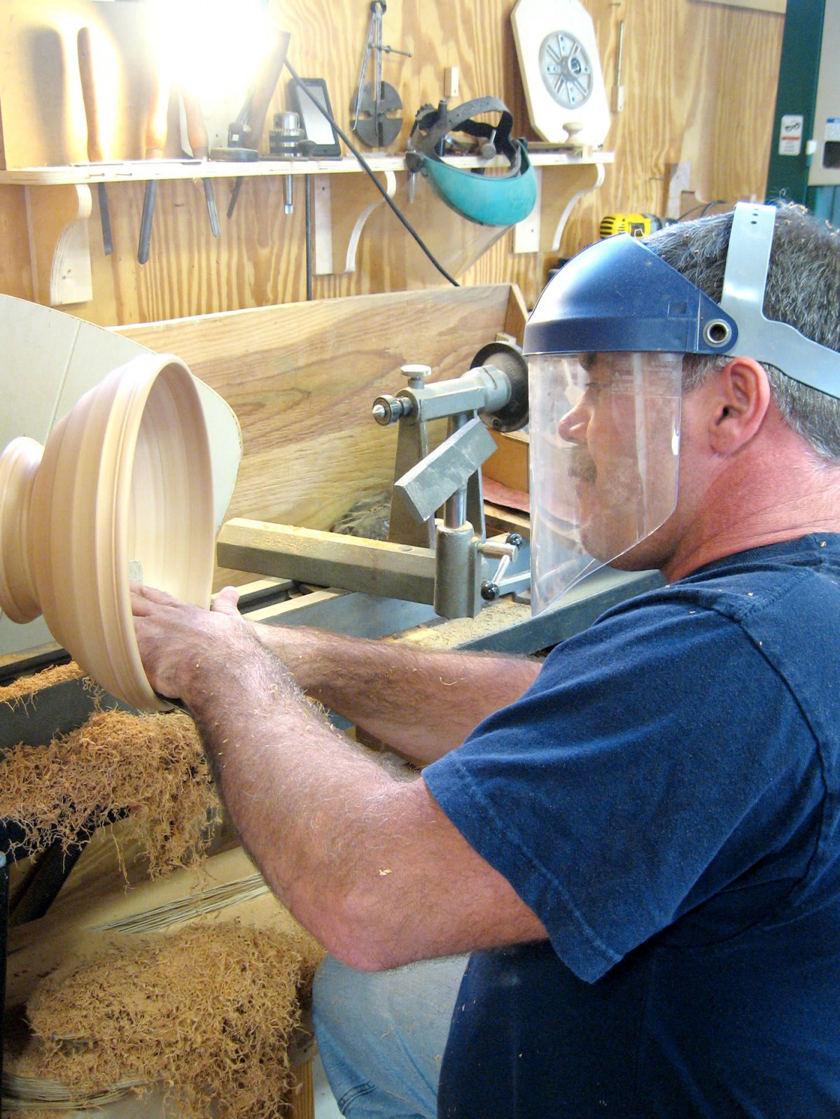 A craftsman using a lathe to shape a wooden bowl, wearing safety gear.