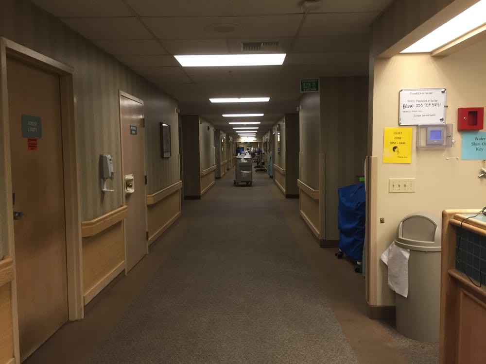A well-lit hospital hallway with a carpeted floor and doors on either side.