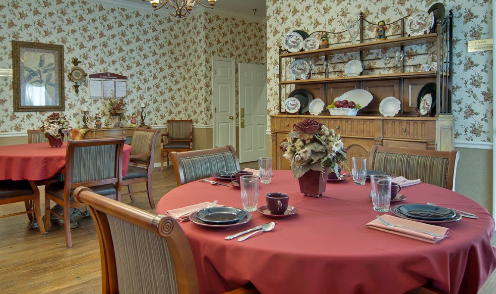 A cozy dining room with a round table set for a meal, featuring floral wallpaper and elegant tableware.